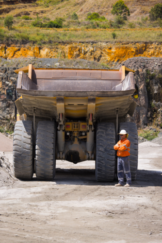 Man with arms crossed standing behind the hauler truck with massive wheels. - Australian Stock Image