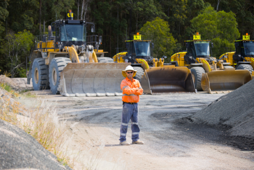 Man with arms crossed standing in between aggregate piles. - Australian Stock Image