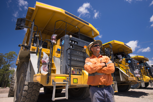 Man with arms crossed standing next to a huge dump truck in a quarry - Australian Stock Image