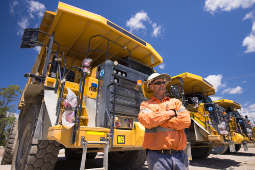 Man with arms crossed standing next to a huge dump truck on mine site - Australian Stock Image