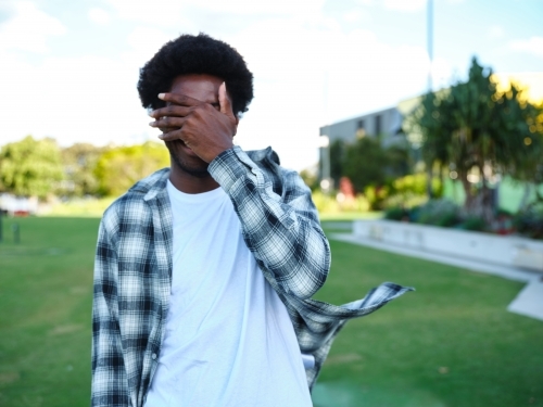 Man with covered face in a park wearing a checkered polo shirt - Australian Stock Image