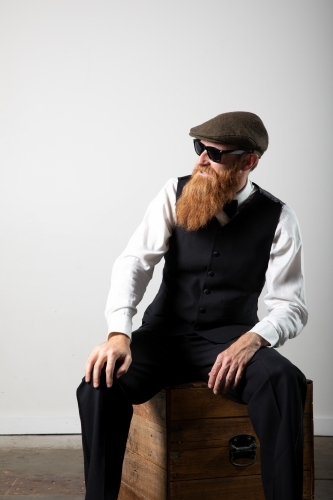 Man with ginger beard and tweed flat cap sitting, posing.