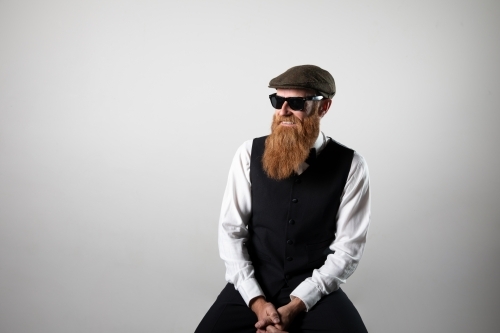 Man with ginger beard and tweed flat cap sitting, posing.