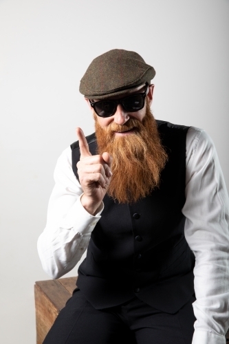 Man with ginger beard and tweed flat cap sitting, posing.