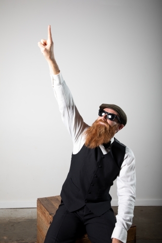 Man with ginger beard and tweed flat cap sitting, posing.