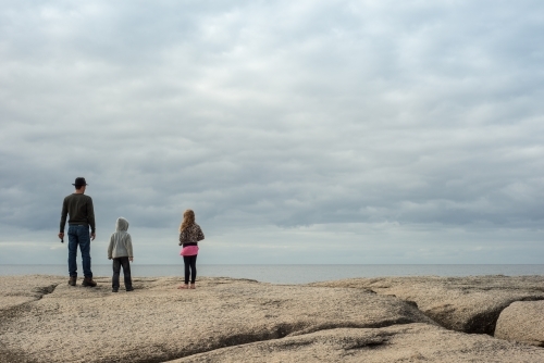 Man with girl and boy on boulder rocks at beach - Australian Stock Image