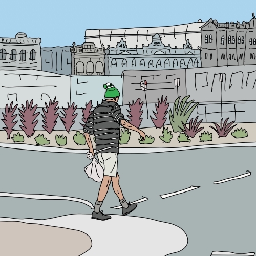 Man with green beanie and bag walking across street with historic buildings in background