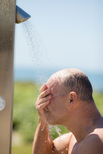 Man with hand across face while taking a shower outside at the beach - Australian Stock Image