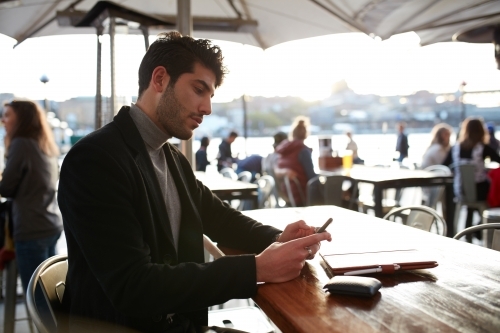 Man working outdoors at cafe with device - Australian Stock Image
