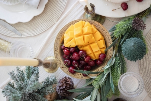 Mango and cherries in bowl on decorated Christmas table - Australian Stock Image