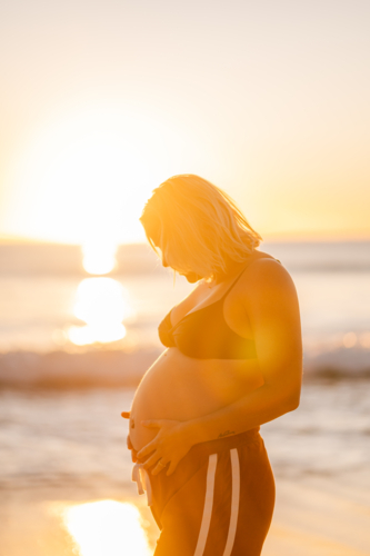 Manly Beach during sunrise with expectant mother cradling baby bump - Australian Stock Image