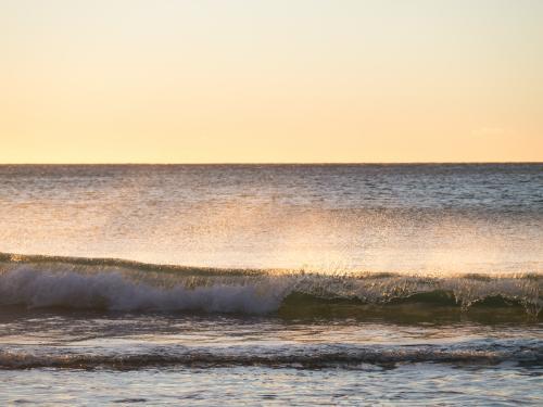 Mare's tail on a ocean wave with sun behind - Australian Stock Image