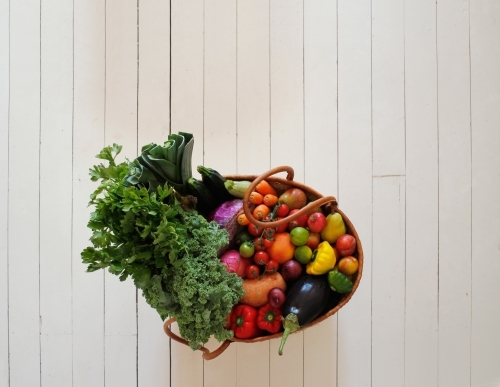 Market basket with fruit and vegetables on white floorboards - Australian Stock Image
