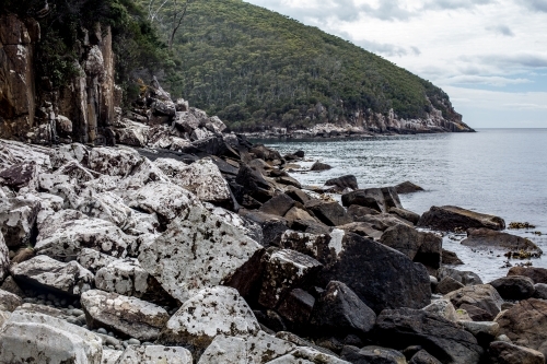 Massive boulders covered in white lichen line the coast  as Cape Hauy rises in the background - Australian Stock Image