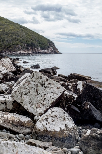 Massive boulders covered in white lichen line the coast  as Cape Hauy rises in the background - Australian Stock Image
