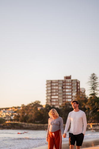 Maternity couple walking hand in hand at Manly Beach during sunrise with peaceful coastal scenery - Australian Stock Image
