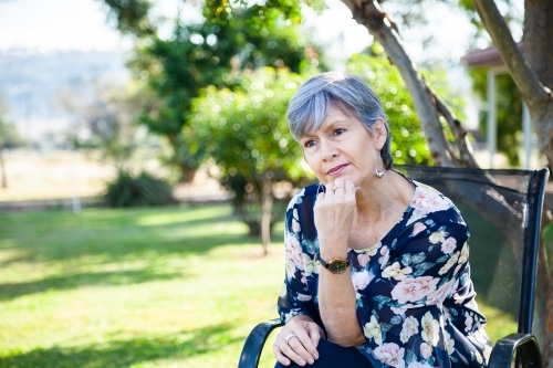 Mature aged woman relaxing in backyard under shady tree - Australian Stock Image