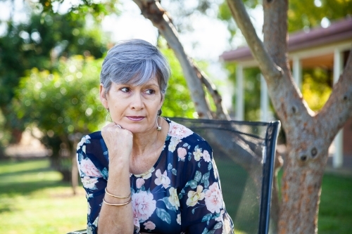 Mature aged woman relaxing in backyard under shady tree - Australian Stock Image