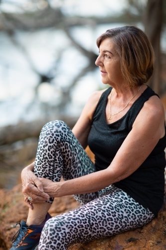 mature lady in activewear sitting in quiet spot by river - Australian Stock Image