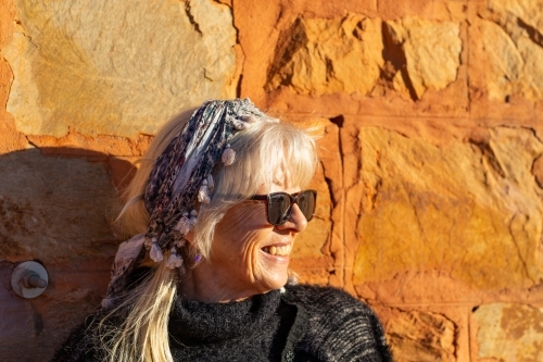 Mature woman head and shoulders against sunlit stone wall - Australian Stock Image