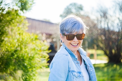 Mature woman in sunnies smiling in the garden - Australian Stock Image
