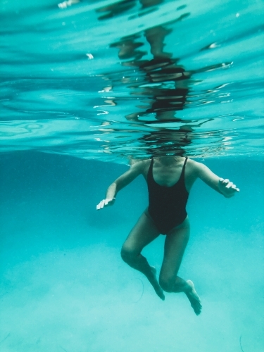Mature woman's athletic body treading water from underwater perspective in ocean - Australian Stock Image