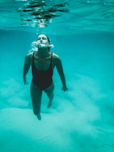 Mature woman's athletic body treading water from underwater perspective in ocean - Australian Stock Image
