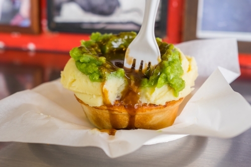 Meat pie topped with mashed potato, peas and gravy