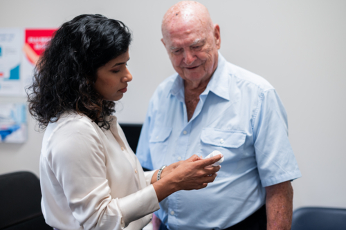 Medical practitioner holds a white medication container while explaining to an elderly man - Australian Stock Image