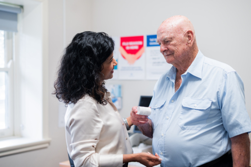 Medical practitioner looking at an elderly man holding medication container inside the clinic - Australian Stock Image