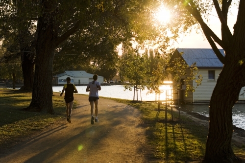 Men running around a lake at sunset - Australian Stock Image