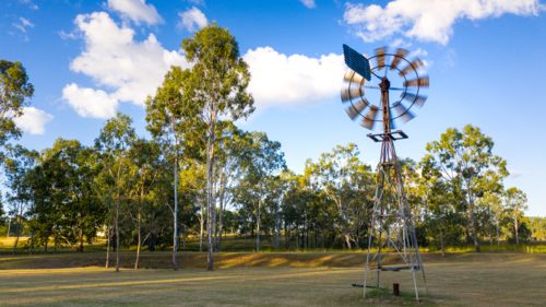 Metal windmill stands prominently in the foreground - Australian Stock Image