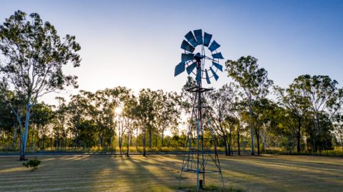 Metal windmill stands prominently in the foreground - Australian Stock Image