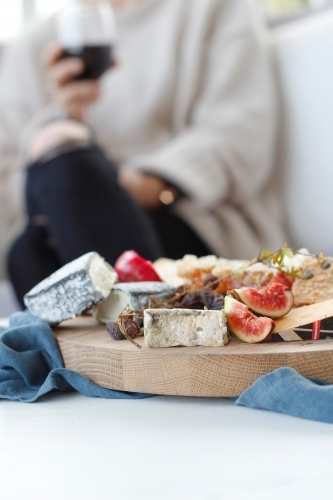 Close up of cheese platter with blurred seated woman holding wine glass in background - Australian Stock Image