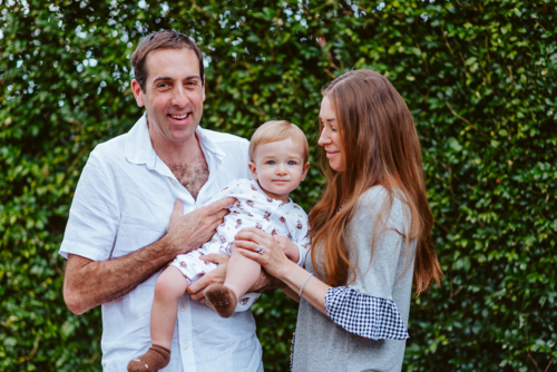 mid aged man and woman holding up a young boy with blond hair in front of a green background - Australian Stock Image