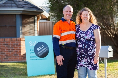 Middle aged couple buy an investment property sold sign in front of house - Australian Stock Image