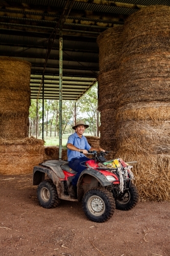 Middle aged farmer on quad bike at farm hay shed collecting feed for cattle - Australian Stock Image