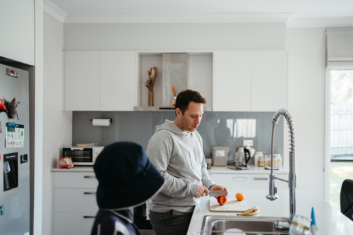 Middle-aged guy cutting fruit for school lunch on the kitchen counter - Australian Stock Image