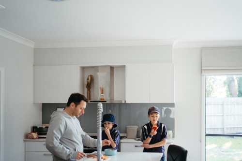 Middle-aged guy cutting fruits on the kitchen counter with the kids. - Australian Stock Image