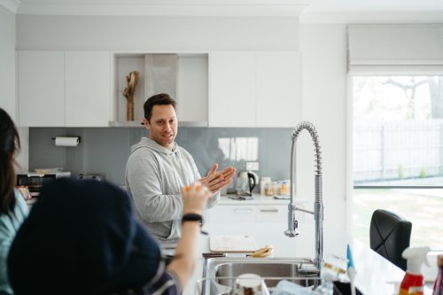 Middle-aged guy standing in the kitchen counter talking about washing hands - Australian Stock Image