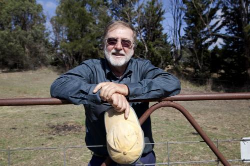 Middle aged male farmer leaning on gate on rural property - Australian Stock Image