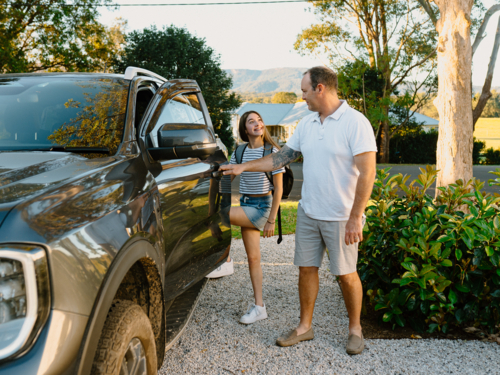 Middle-aged man opening the car door to a young teenage girl. - Australian Stock Image