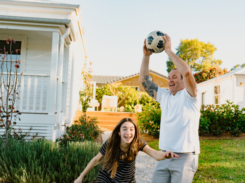 Middle aged man playing by home with teen daughter catching soccer ball - Australian Stock Image