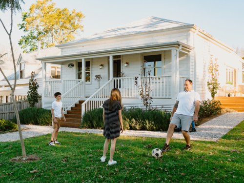 Middle aged man playing soccer with his kids in their front yard. - Australian Stock Image