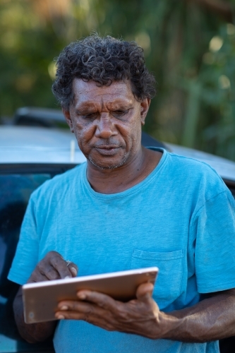 middle-aged man standing typing on digital tablet - Australian Stock Image