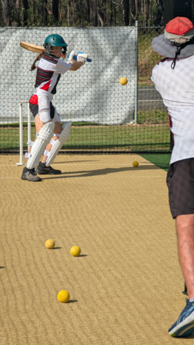 Middle-aged man throwing cricket balls to female batter. - Australian Stock Image