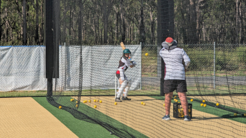 Middle-aged person throwing cricket balls to young female batter - Australian Stock Image