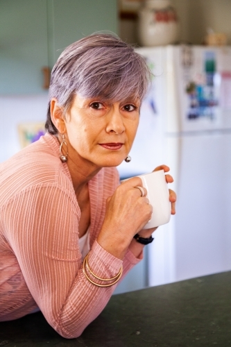 Middle aged woman drinking a cup of tea in her kitchen