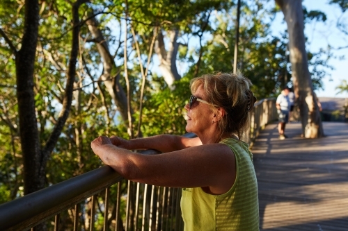 Middle aged woman leaning on a fence looking out at a view - Australian Stock Image