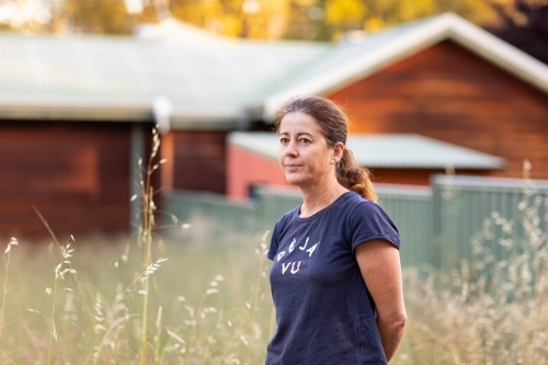 middle-aged woman outside with rustic house and wild oats in background - Australian Stock Image